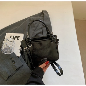 Detail der schwarzen Lackleder-Eimertasche mit silbernem COIN 2DN Logo und Faltenstruktur