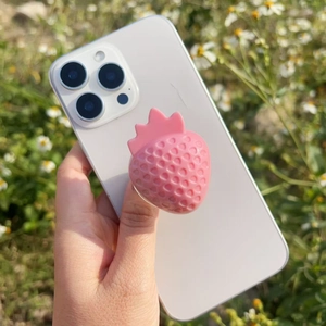 Close-up of pink 3D strawberry phone grip on a white smartphone held in a hand