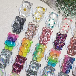 Flat lay of colorful resin bear phone grips with dried flowers and glitter accents