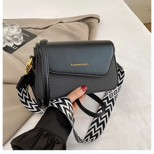 Detail of black square bag with woven texture, metal chain, and stylish patterned strap
