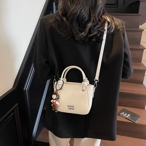Minimalistische cremeweiße Beuteltasche mit Anhänger, getragen von einem Model