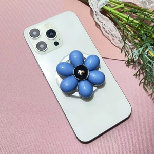 Close-up of a blue flower phone grip with a gold heart center on a white phone