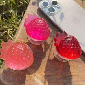 Three gradient strawberry resin phone grips in pink and red on a rustic wooden table