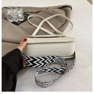 Detail of a creamy white crossbody bag featuring stylish dual shoulder straps and gold hardware