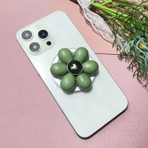Macro detail of glossy olive green flower phone grip with golden heart center on pink fabric