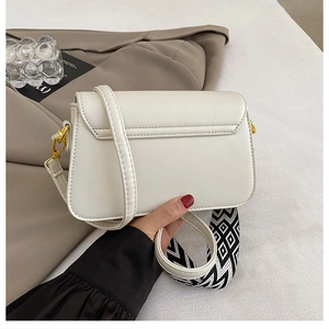 Detail of white square bag featuring a gold metal clasp and a woven geometric shoulder strap