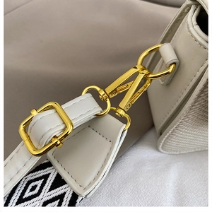 Close-up of golden hardware and black and white woven strap on cream shoulder bag