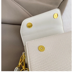 Detail of cream woven texture handbag featuring gold magnetic clasps and side lobster hook