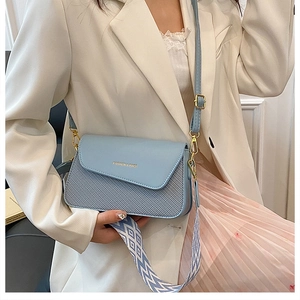 Detail of light blue flap bag featuring golden text and geometric woven shoulder strap