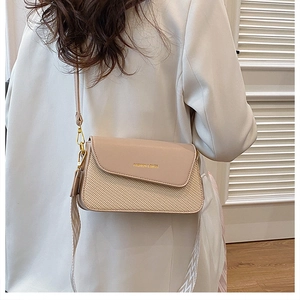 Detail of a beige leather and straw crossbody bag worn over a white suit jacket