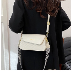 Detail of cream square bag with gold text, featuring a leather strap and geometric webbing