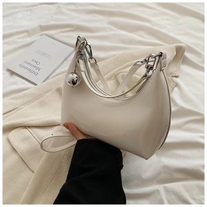 Détail du sac croissant blanc brillant avec un grand pendentif boule argentée sur le zip