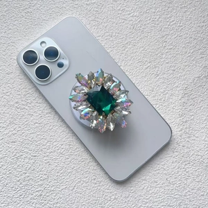 Macro detail of luxury magnetic phone grip with green gemstone and diamond inlay