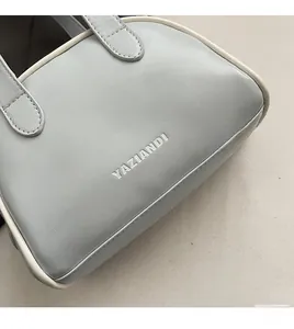 Détail du sac bowling en cuir gris-bleu avec logo embossé et finitions de passepoil blanc