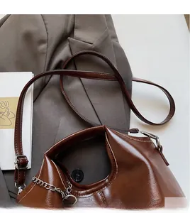 Detailed close-up of brown glossy leather shoulder bag with adjustable strap and chain