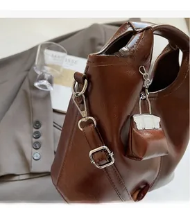 Detail of dark brown glossy leather tote with silver hardware and mini charm