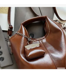 Detail of dark brown oily leather tote bag with contrast stitching and mini bag charm