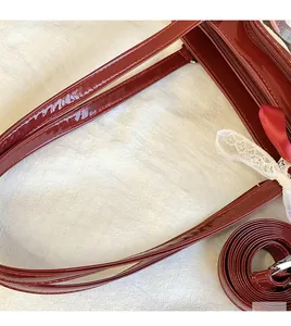 Detail of burgundy patent leather bag with long handles and lace bow accent