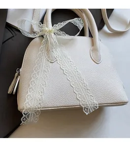 Détail du sac coquille en cuir litchi blanc avec nœud en dentelle et zip métallique
