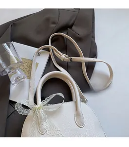 Détail d'un sac à main blanc en cuir litchi avec nœud en dentelle et bandoulière