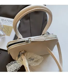 Détail du zip argenté et du nœud en dentelle sur le sac à main en cuir beige clair