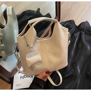 Detailed view of cream leather tote bag with mini charm and adjustable strap on a mirror