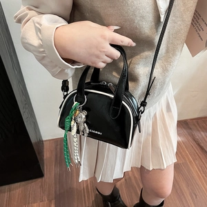 Sac bowling noir chic avec liseré blanc, bandoulière réglable et breloque ours sur modèle