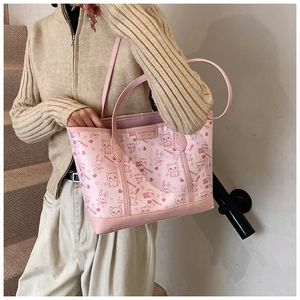 Pink tote bag detail with cute cartoon prints and branded metal plaque on the front