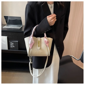 Gros plan sur un sac seau en cuir crème avec anse en foulard et fermoir doré