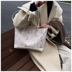 Detail of a beige tote bag featuring cute animal prints and a leather brand patch