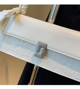 Detailed close-up of white leather handbag featuring geometric embossing and a crystal lock