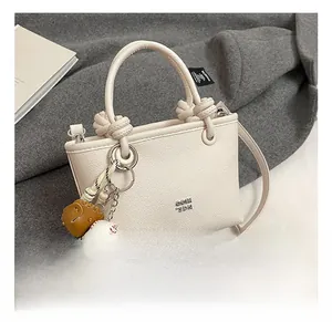 Detail of cream lychee texture leather bucket bag with knotted rope handle and baseball charm