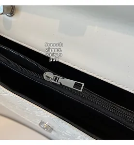 Detailed close-up of smooth silver zipper and neat stitching on a white leather handbag
