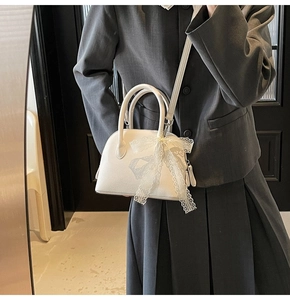 Détail d'un sac à main blanc en forme de coquille avec un nœud en dentelle délicat