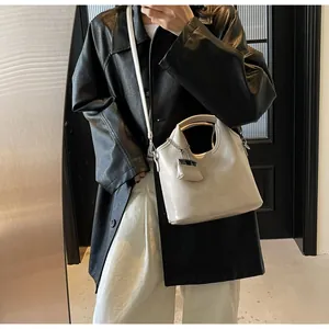Detail of cream leather tote bag featuring unique metal circular handle and chic chain decor