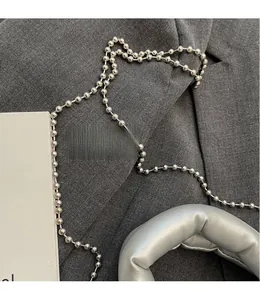 Detail of smooth silver bead shoulder strap and metallic handle charm on gray fabric