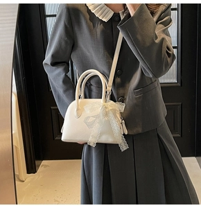 Détail d'un sac à main blanc en cuir litchi avec un nœud en dentelle délicat et forme coquille