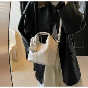 Close-up of beige glossy leather tote bag with small chain charm on a model