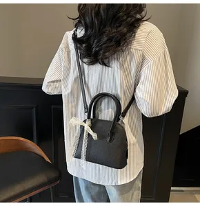 Détail d'un sac à main en cuir noir grainé avec un nœud en dentelle blanche sur modèle