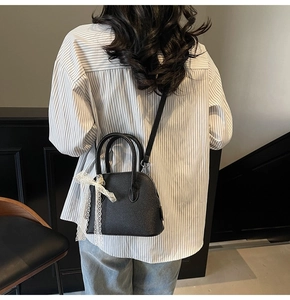 Détail d'un sac à main en cuir grainé noir avec nœud en dentelle blanche et pieds en métal
