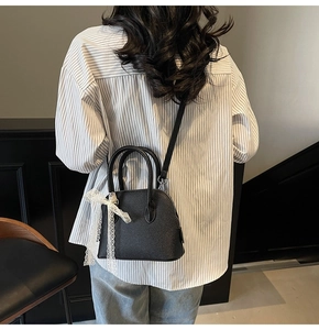 Détail du mini sac noir en cuir grainé avec un nœud décoratif en dentelle blanche