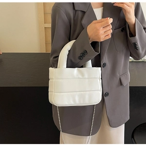 Detail of white quilted puffy handbag with silver ball chain strap on a grey suit jacket