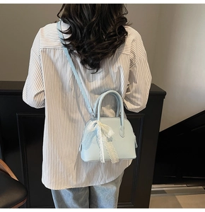 Détail d'un sac à main bleu clair avec motif litchi, nœud en dentelle et bandoulière