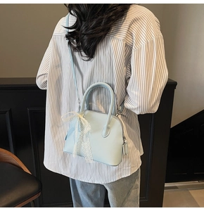 Détail d'un sac à main bleu clair avec motif litchi, nœud en dentelle et bandoulière