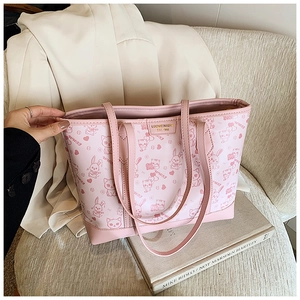 Close-up of pink tote bag with cartoon print and gold logo tag on a soft sofa
