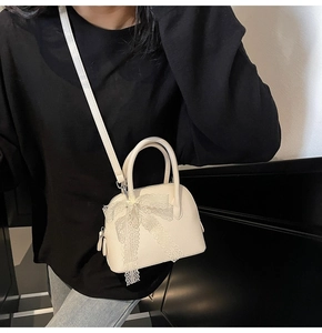 Détail d'un petit sac blanc en forme de coquillage avec nœud en dentelle et cuir grainé