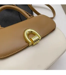 Detail of two-tone leather shoulder bag with gold horseshoe buckle and brown strap