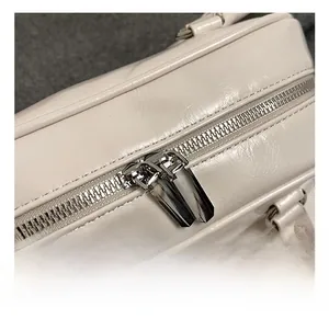 Close-up of premium cream leather texture and shiny silver dual metal zippers on the bag
