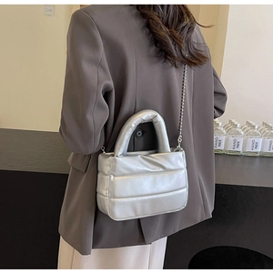 Detail of silver quilted puffer bucket bag featuring metallic texture and chain strap