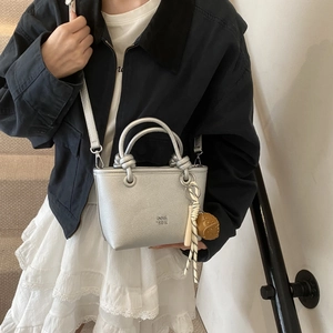Detail of silver matte bucket bag with knot handle and braided rope charm accessory